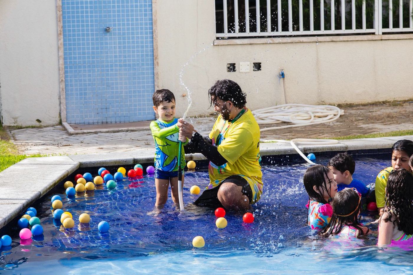 Recreador brincando com criança de mangueira na piscina cheia de bolinhas coloridas